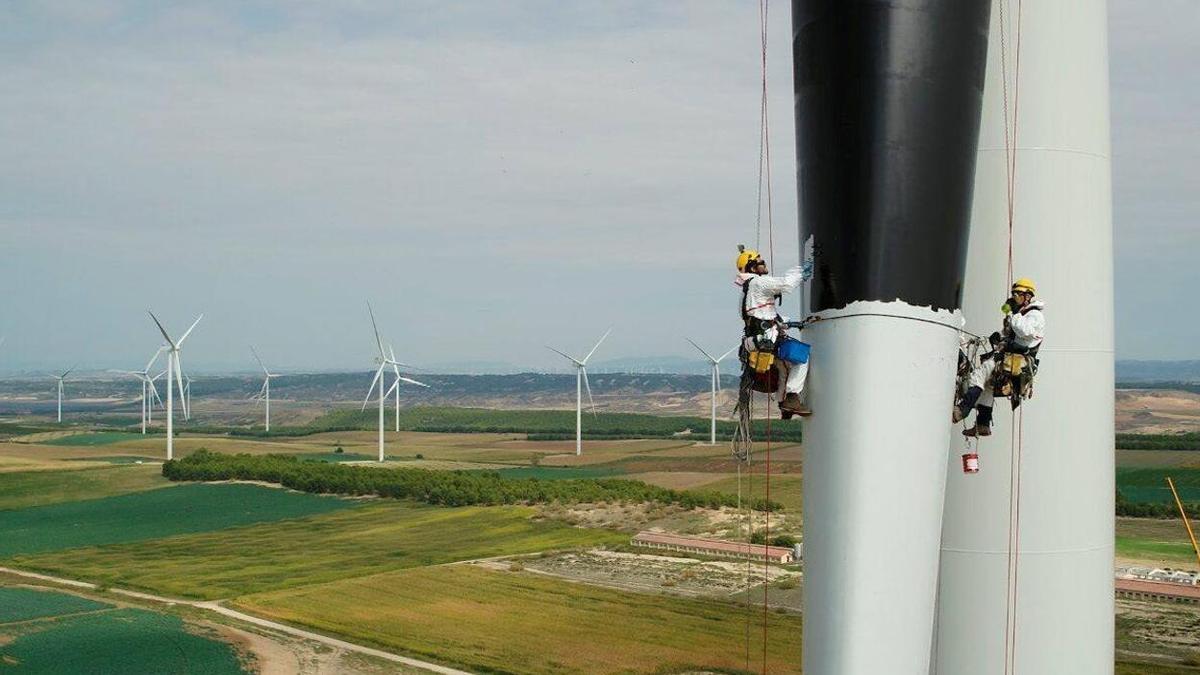 Dos operarios pimtan de negro una pala de un aerogenerador de Iberdrola.
