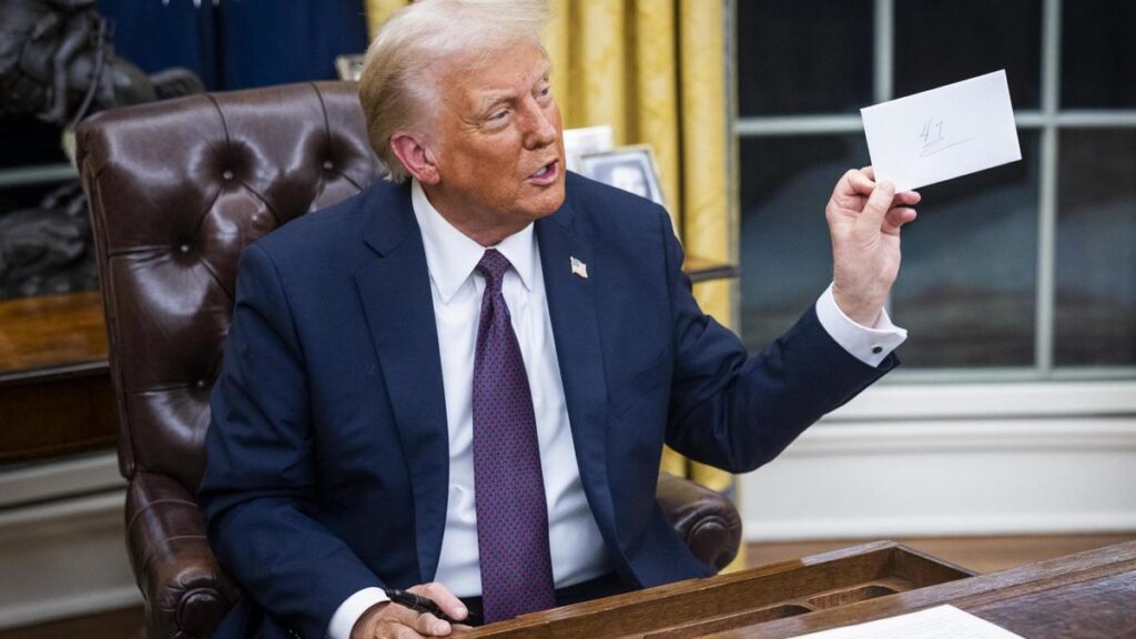 Trump, en el Despacho Oval, sujeta una carta que el expresidente Biden dejó en el escritorio para él.