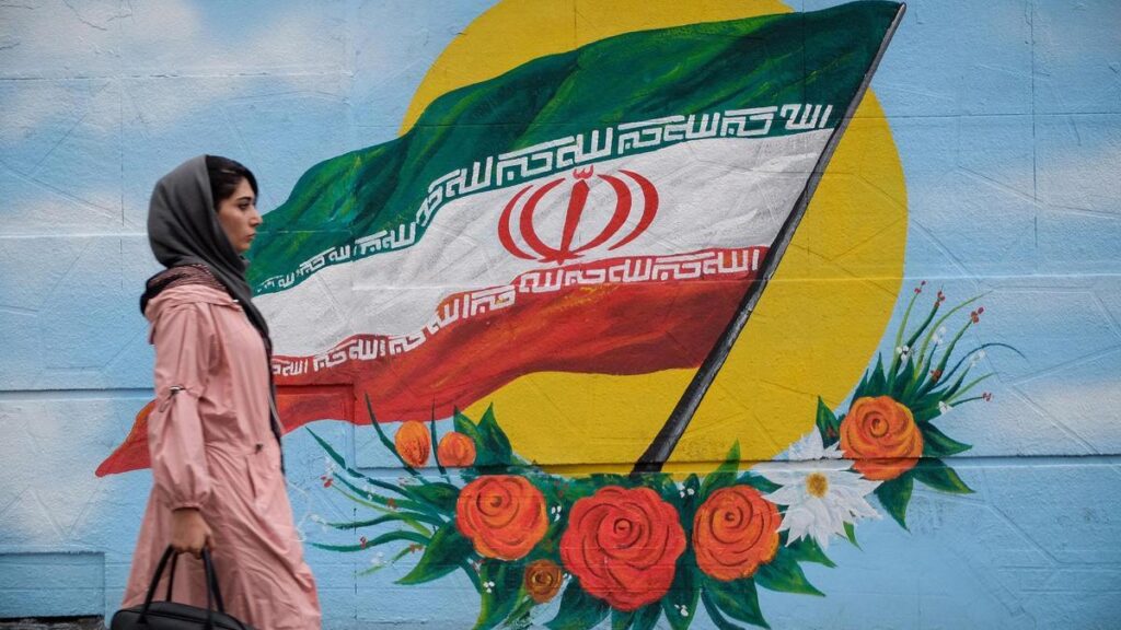 Archivo - Una mujer camina frente a un mural con la bandera de Irán situado en una de las calles de Teherán