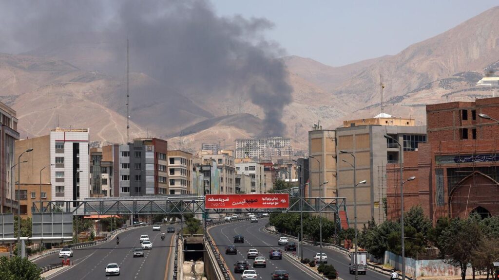 Vehículos circulan por una autopista mientras se eleva humo al fondo desde una refinería de petróleo, al noroeste de Teherán.