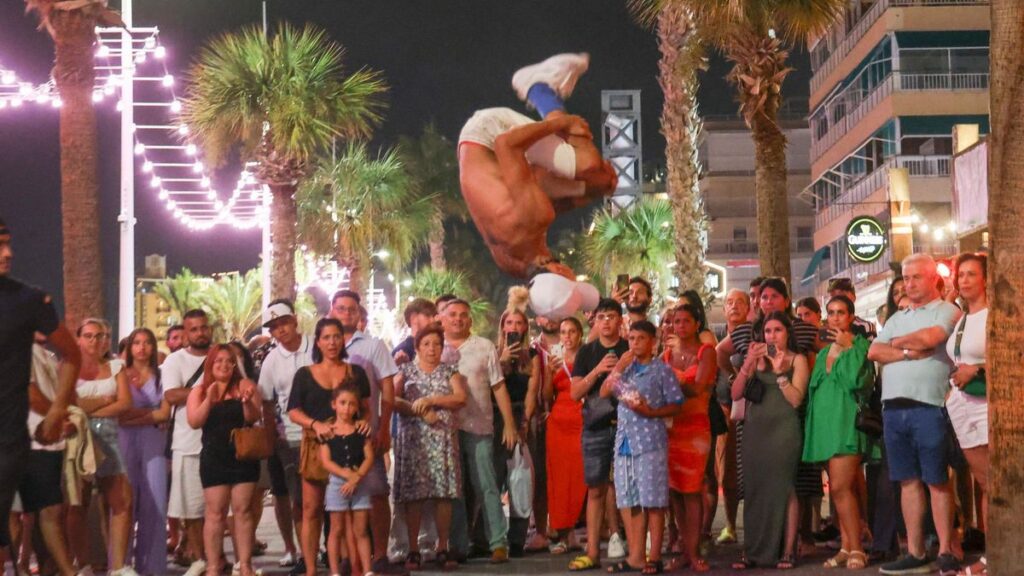 Turistas en la playa de Levante de Benidorm observan a un artista callejero, en una imagen de archivo