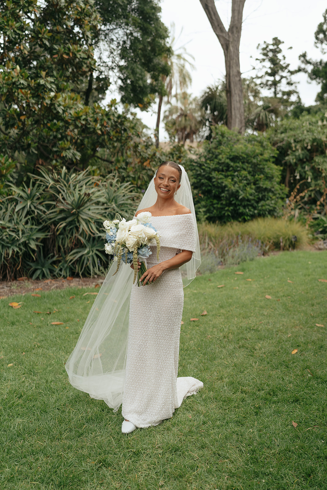 Mariée en robe bustier Rosa Clara tenant un bouquet bleu et blanc avec des fleurs fruitées lors d'un mariage dans le jardin
