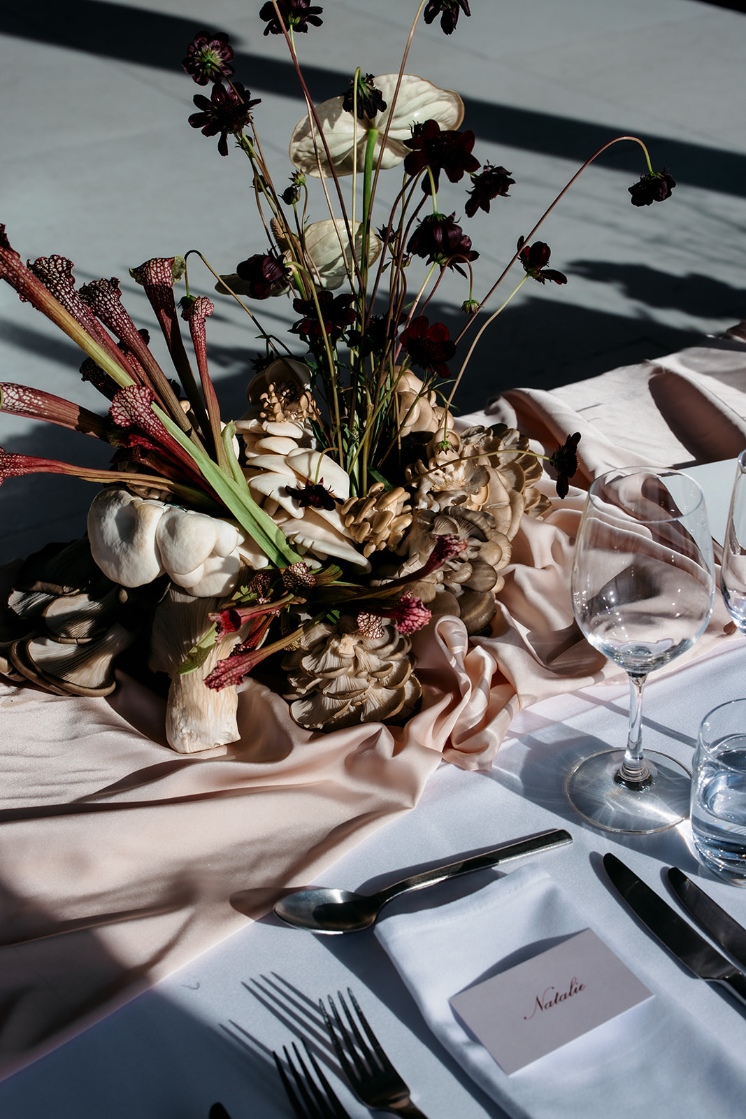 Gros plan d'une pièce maîtresse unique de réception de mariage de champignons sauvages et de sarracenia avec des fleurs bordeaux foncés et des pleurotes sur une nappe en soie blush à Marnong Estate Winery, fleurs de The Beautiful Bunch, photographie de Kinship de Kristy